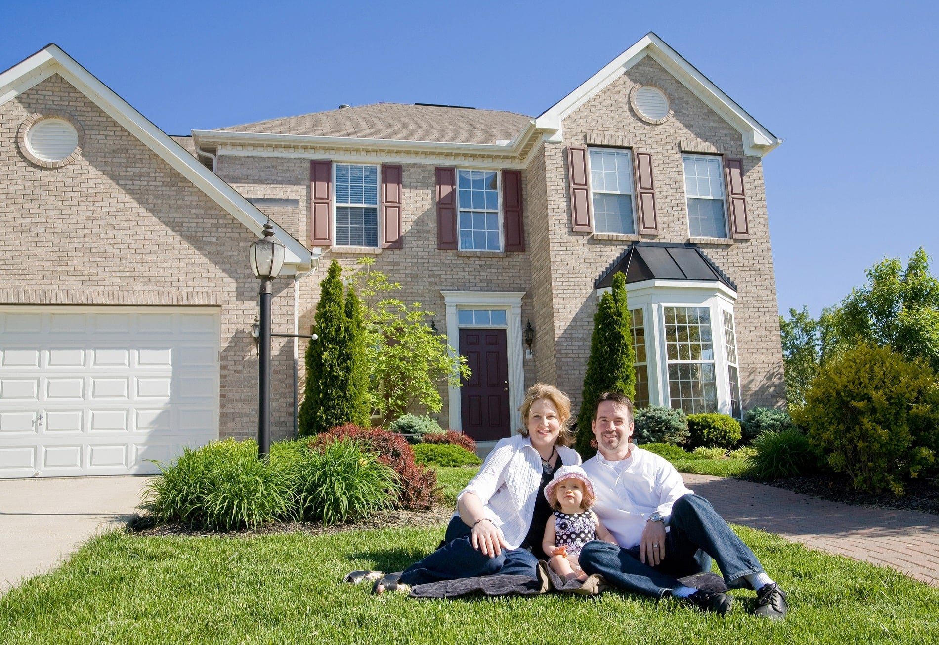 A happy family sitting on the lawn in front of a large, two-story home.