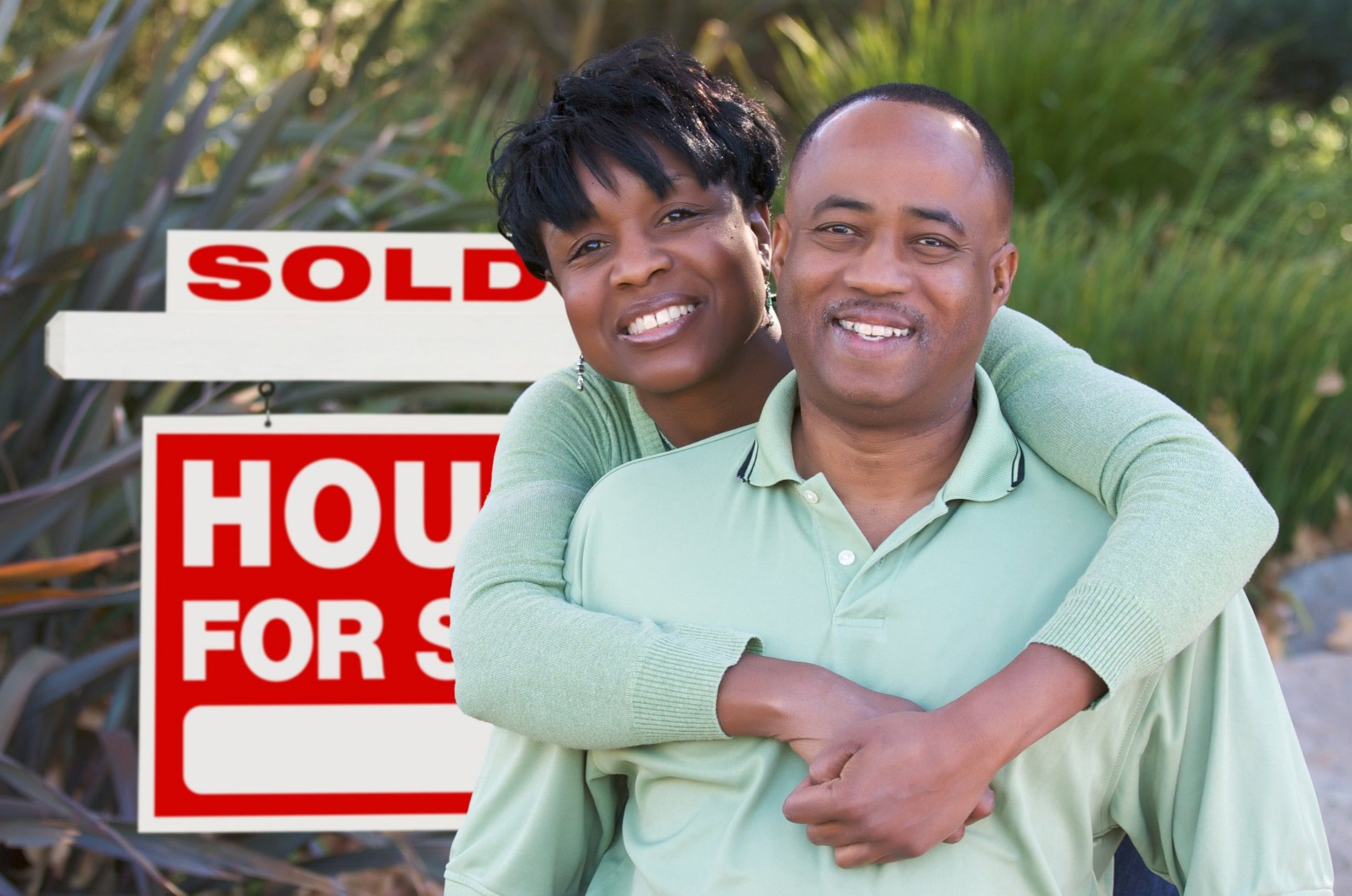 A happy couple in front of a sold house sign
